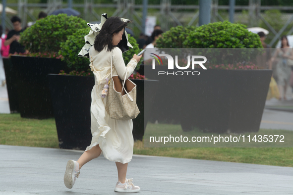 People are trying to hold umbrellas in a big wind in front of the International Expo Center in Shanghai, China, on July 26, 2024. 