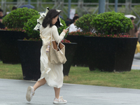 People are trying to hold umbrellas in a big wind in front of the International Expo Center in Shanghai, China, on July 26, 2024. (