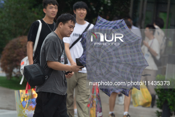 People are trying to hold umbrellas in a big wind in front of the International Expo Center in Shanghai, China, on July 26, 2024. 