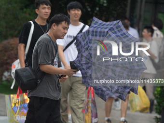 People are trying to hold umbrellas in a big wind in front of the International Expo Center in Shanghai, China, on July 26, 2024. (