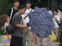 People are trying to hold umbrellas in a big wind in front of the International Expo Center in Shanghai, China, on July 26, 2024. (