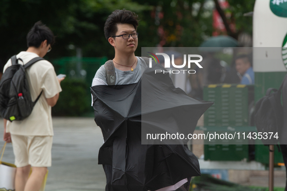 People are trying to hold umbrellas in a big wind in front of the International Expo Center in Shanghai, China, on July 26, 2024. 