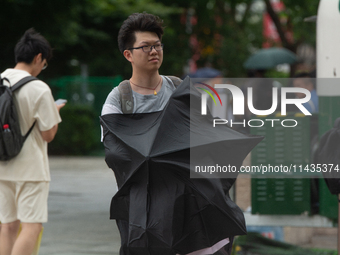 People are trying to hold umbrellas in a big wind in front of the International Expo Center in Shanghai, China, on July 26, 2024. (