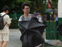 People are trying to hold umbrellas in a big wind in front of the International Expo Center in Shanghai, China, on July 26, 2024. (