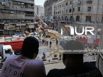 Pedestrians in a building are looking at the fire after the firefighters of the Civil Defense are controlling a huge fire that broke out in...