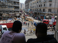 Pedestrians in a building are looking at the fire after the firefighters of the Civil Defense are controlling a huge fire that broke out in...