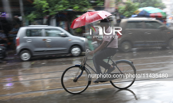 A man is riding his bicycle with an umbrella on a road during heavy monsoon rain in Kolkata, India, on July 26, 2024. 