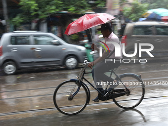 A man is riding his bicycle with an umbrella on a road during heavy monsoon rain in Kolkata, India, on July 26, 2024. (