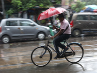 A man is riding his bicycle with an umbrella on a road during heavy monsoon rain in Kolkata, India, on July 26, 2024. (