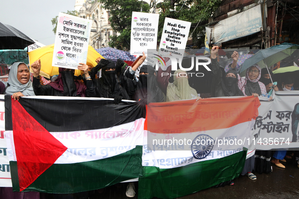 Muslim women are wearing hijabs, showing a slogan, and holding posters along with Palestine and Indian National Flags during a protest rally...