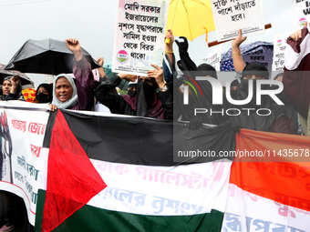 Muslim women are wearing hijabs, showing a slogan, and holding posters along with Palestine and Indian National Flags during a protest rally...