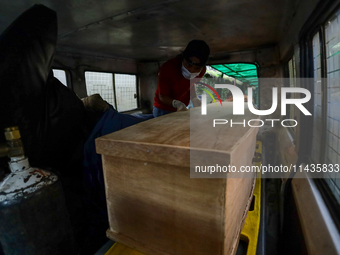 Dead body management officials are loading a coffin containing the body of a deceased in the Saurya Airlines crash into a hearse at a morgue...