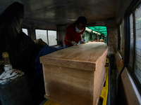 Dead body management officials are loading a coffin containing the body of a deceased in the Saurya Airlines crash into a hearse at a morgue...