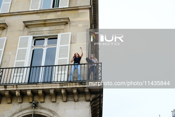 Two women are dancing on their balcony in front of the queues of people waiting to attend the opening ceremony of the Olympic Games. 