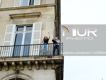 Two women are dancing on their balcony in front of the queues of people waiting to attend the opening ceremony of the Olympic Games. (