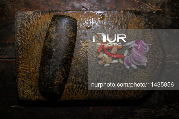 A woman is pounding masala in a heavy Shil Nora (Batan and Una) in Tehtatta, West Bengal, India, on July 15, 2024. 