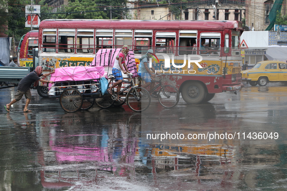 A cycle-van puller is covering with a plastic sheet and peddling through a busy street as it is raining in Kolkata, India, on July 26, 2024....