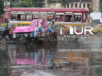 A cycle-van puller is covering with a plastic sheet and peddling through a busy street as it is raining in Kolkata, India, on July 26, 2024....