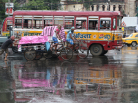 A cycle-van puller is covering with a plastic sheet and peddling through a busy street as it is raining in Kolkata, India, on July 26, 2024....