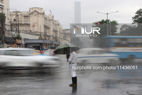 A traffic police officer is holding an umbrella and controlling the traffic system during the monsoon rainfall on a busy road in Kolkata, In...