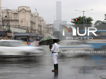 A traffic police officer is holding an umbrella and controlling the traffic system during the monsoon rainfall on a busy road in Kolkata, In...