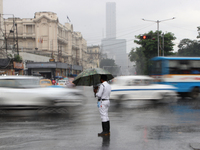 A traffic police officer is holding an umbrella and controlling the traffic system during the monsoon rainfall on a busy road in Kolkata, In...