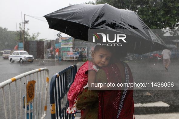 The mother is carrying her child in her arms and protecting her child with an umbrella in the monsoon rain in Kolkata, India, on July 26, 20...