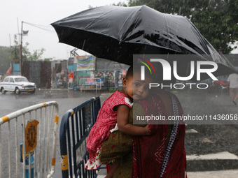 The mother is carrying her child in her arms and protecting her child with an umbrella in the monsoon rain in Kolkata, India, on July 26, 20...