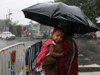 The mother is carrying her child in her arms and protecting her child with an umbrella in the monsoon rain in Kolkata, India, on July 26, 20...