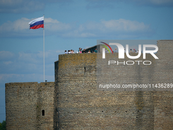 Visitors are seen on a tower of the Ivangorod Fortress with a Russian flag flying accross the river in Narva, Estonia on 24 July, 2024. Esto...