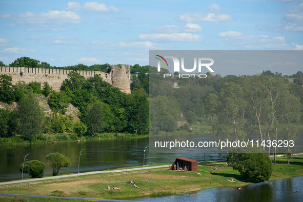 People are seen sunbathing on the banks of the Narva River in Narva, Estonia on 24 July, 2024. Estonian authorities have closed the bridge t...