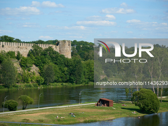 People are seen sunbathing on the banks of the Narva River in Narva, Estonia on 24 July, 2024. Estonian authorities have closed the bridge t...