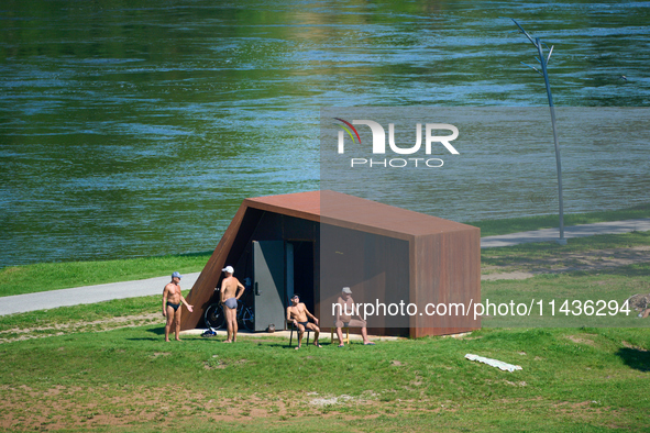 People are seen sunbathing on the banks of the Narva River in Narva, Estonia on 24 July, 2024. Estonian authorities have closed the bridge t...