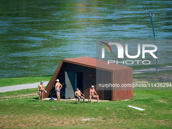 People are seen sunbathing on the banks of the Narva River in Narva, Estonia on 24 July, 2024. Estonian authorities have closed the bridge t...