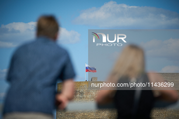 People look on as a Russian flag flies on the Ivangorod Fortress in Narva, Estonia on 24 July, 2024. Estonian authorities have closed the br...