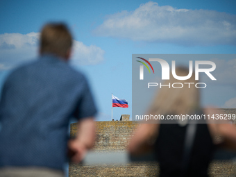 People look on as a Russian flag flies on the Ivangorod Fortress in Narva, Estonia on 24 July, 2024. Estonian authorities have closed the br...