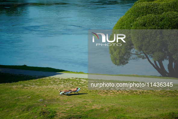 A man is seen sunbathing on the Narva River in Narva, Estonia on 24 July, 2024. Estonian authorities have closed the bridge that connects Ru...