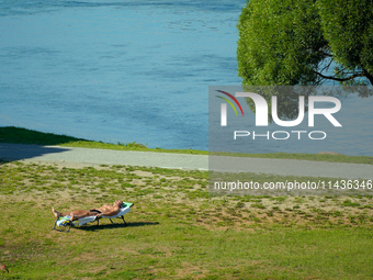 A man is seen sunbathing on the Narva River in Narva, Estonia on 24 July, 2024. Estonian authorities have closed the bridge that connects Ru...