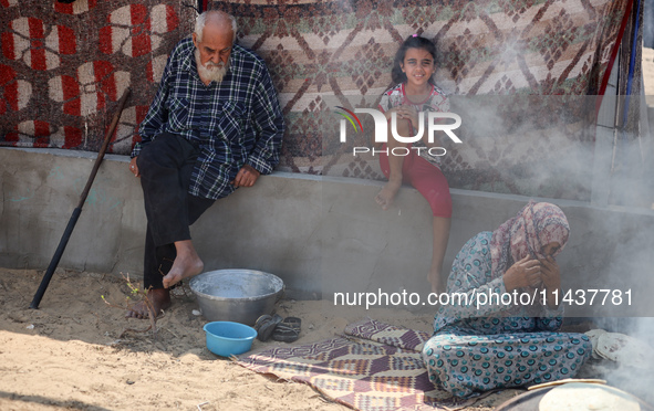 Displaced Palestinians from the eastern part of Khan Yunis are preparing to cook at a temporary camp set up in the grounds of a cemetery in...