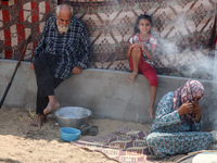 Displaced Palestinians from the eastern part of Khan Yunis are preparing to cook at a temporary camp set up in the grounds of a cemetery in...