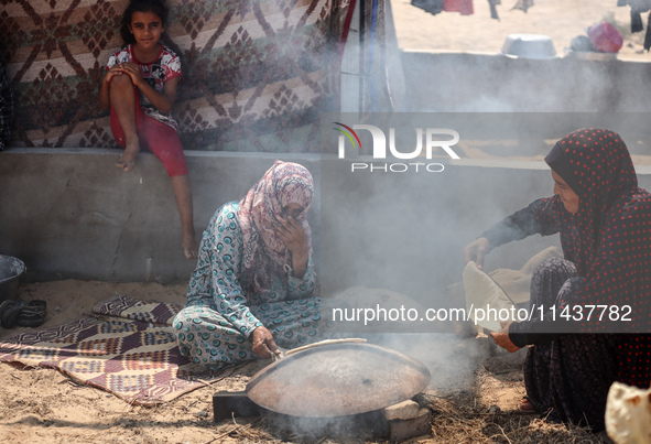 Displaced Palestinians from the eastern part of Khan Yunis are preparing to cook at a temporary camp set up in the grounds of a cemetery in...