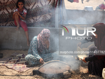 Displaced Palestinians from the eastern part of Khan Yunis are preparing to cook at a temporary camp set up in the grounds of a cemetery in...