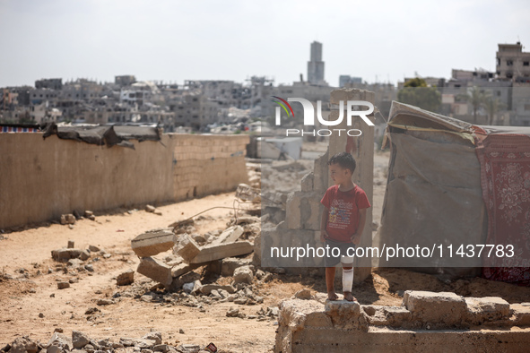 A boy is standing next to graves as displaced Palestinians from the eastern part of Khan Yunis are setting up a temporary camp in the ground...