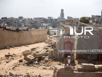 A boy is standing next to graves as displaced Palestinians from the eastern part of Khan Yunis are setting up a temporary camp in the ground...