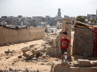 A boy is standing next to graves as displaced Palestinians from the eastern part of Khan Yunis are setting up a temporary camp in the ground...