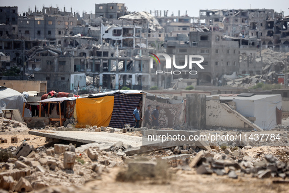 People are walking next to graves as displaced Palestinians from the eastern part of Khan Yunis are setting up a temporary camp in the groun...