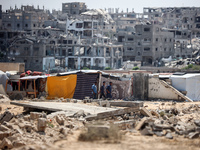 People are walking next to graves as displaced Palestinians from the eastern part of Khan Yunis are setting up a temporary camp in the groun...