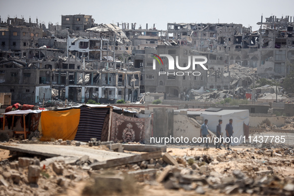 People are walking next to graves as displaced Palestinians from the eastern part of Khan Yunis are setting up a temporary camp in the groun...