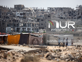 People are walking next to graves as displaced Palestinians from the eastern part of Khan Yunis are setting up a temporary camp in the groun...