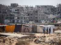 People are walking next to graves as displaced Palestinians from the eastern part of Khan Yunis are setting up a temporary camp in the groun...